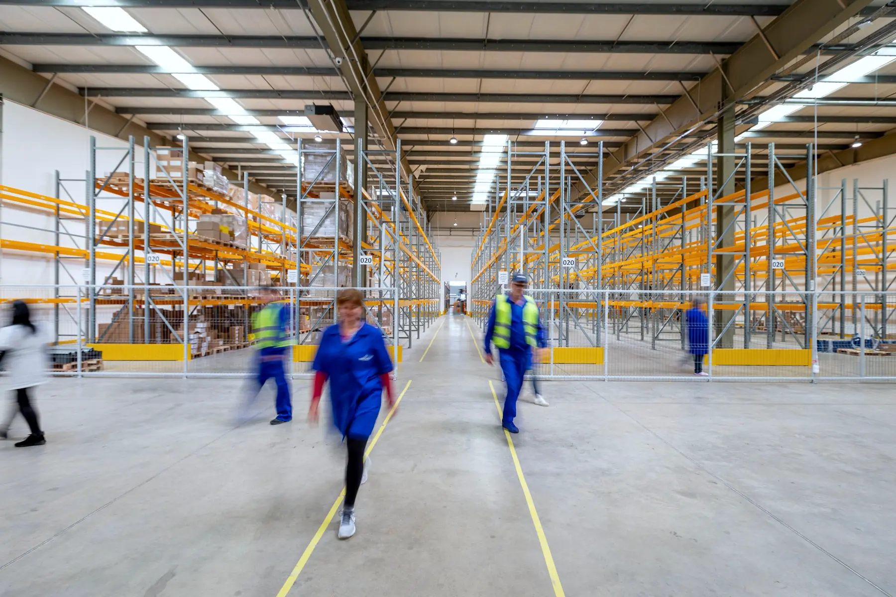 Staff moving through a long warehouse aisle lined with racking