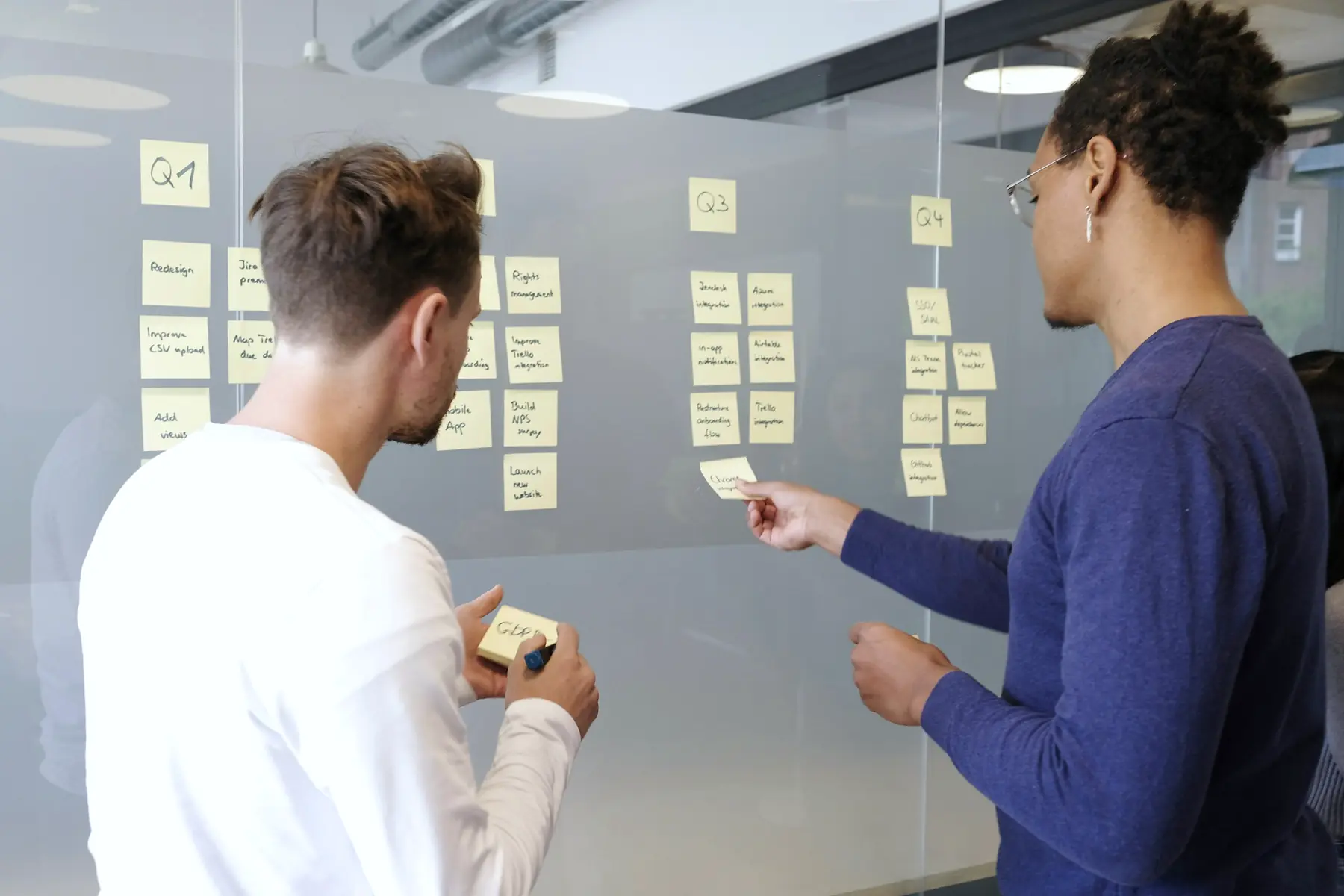 Two colleagues planning the quarter's work on sticky notes at a glass wall